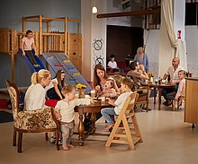 Kindercafe Kindercafe: Kinder sitzen am Tisch mit Ihren Eltern. es wird gegessen und getrunken. Ein Mädchen ist gerade auf der Rutsche.