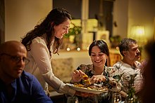 Event Location & Catering – Kindercafe Essen: Kellnerin serviert einer Gästin am Tisch Kuchen – beide lächeln.