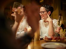 Event-Location & Catering: Frau sitzt am Tisch, trinkt etwas und lacht.