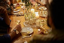 Das Anna Event-Location & Catering: Nahaufnahme eines schön dekorierten Tisch bei einem Abend-Event, bei dem die Gäste gerade miteinander reden, Sekt trinken und Vorspeisen essen.