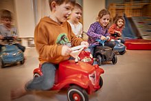 Keline Mädchen und Jungs fahren ein Rennen mit Bobbycars in der Spielecke.
